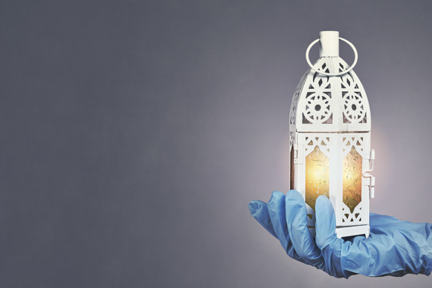 Hand in protective medical gloves holding traditional Arabic lantern with middle-eastern carving. Celebrating Holly month Ramadan 2020 in quarantine. A doctor celebrates Ramadan in hospital
